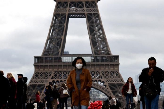 Một du khách đeo mặt nạ bảo vệ khi đi bộ phía trước tháp Eiffel, Paris vào 1/2, giữa mùa Covid-19 bùng phát. Ảnh: Reuters.