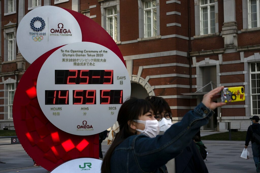 Người dân chụp ảnh với đồng hồ đếm ngược Olympic 2020, hiển thị ngày giờ hiện tại bên ngoài ga Tokyo. Đại dịch coronavirus đã buộc phải hoãn Thế vận hội. Ảnh: Jae C Hong / AP