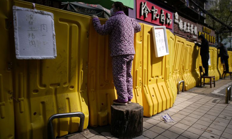 Người dân Vũ Hán đứng lên ghế để mua đồ qua hàng rào phong tỏa ngày 1/4. Ảnh: Reuters.